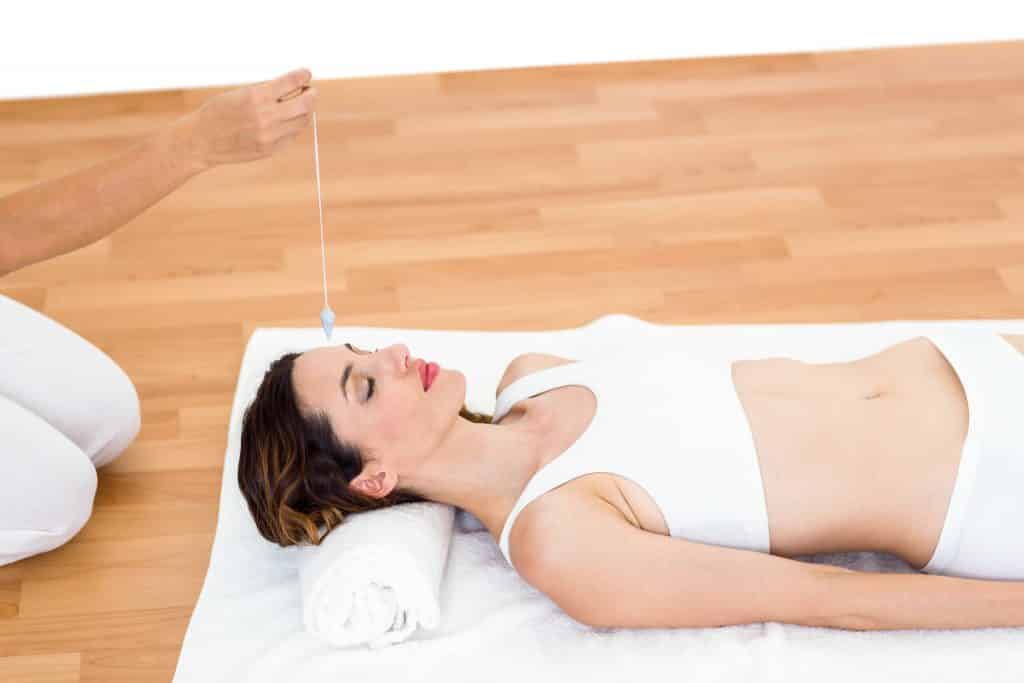 Imagem de uma mulher vestida com roupa branca deitada sobre o chão de piso de madeira sobre uma toalha. Ela está fazendo uma sessão de hipnoterapia.