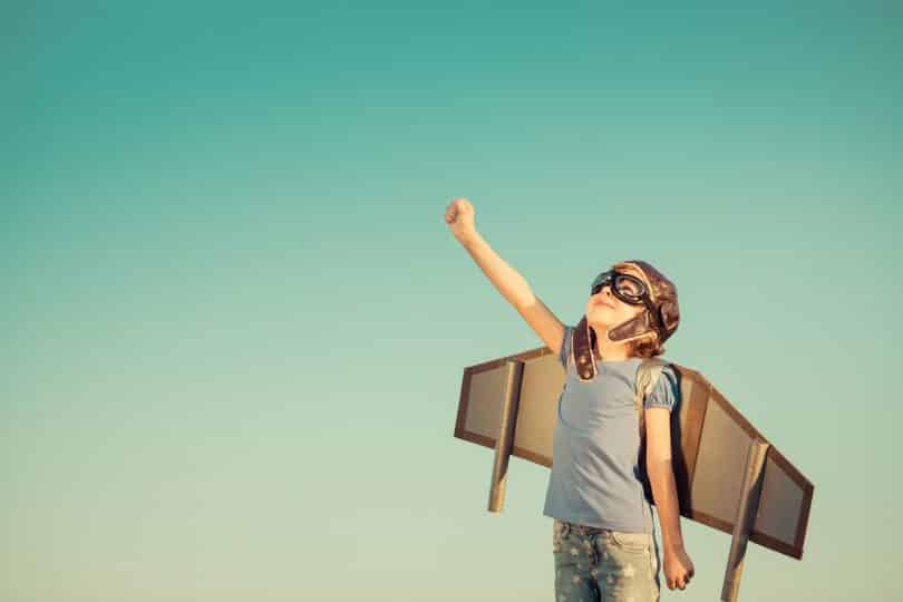 Criança feliz brincando com asas de brinquedo em fundo de céu de verão.