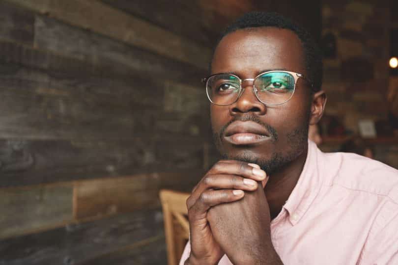 Jovem negro de camisa rosa. Está sentado pensando enquanto olha para frente