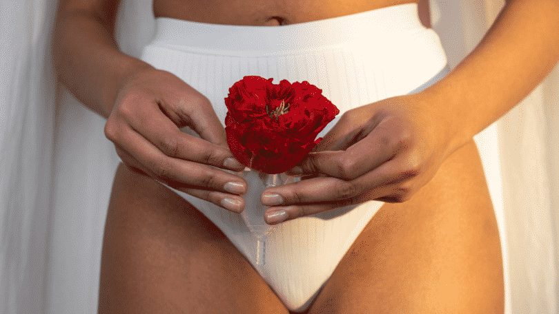 Mulher usando roupa de baixo branca segurando a flor vermelha em um copo menstrual