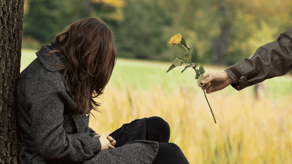 Pessoa oferecendo uma flor amarela como pedido desculpas para mulher cabisbaixa