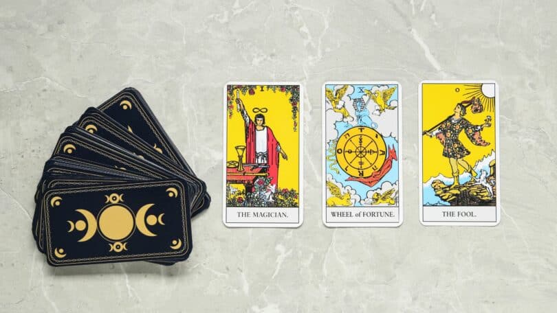 Imagem de cartas de tarot em cima de uma mesa, algumas viradas para cima e o baralho virado para baixo