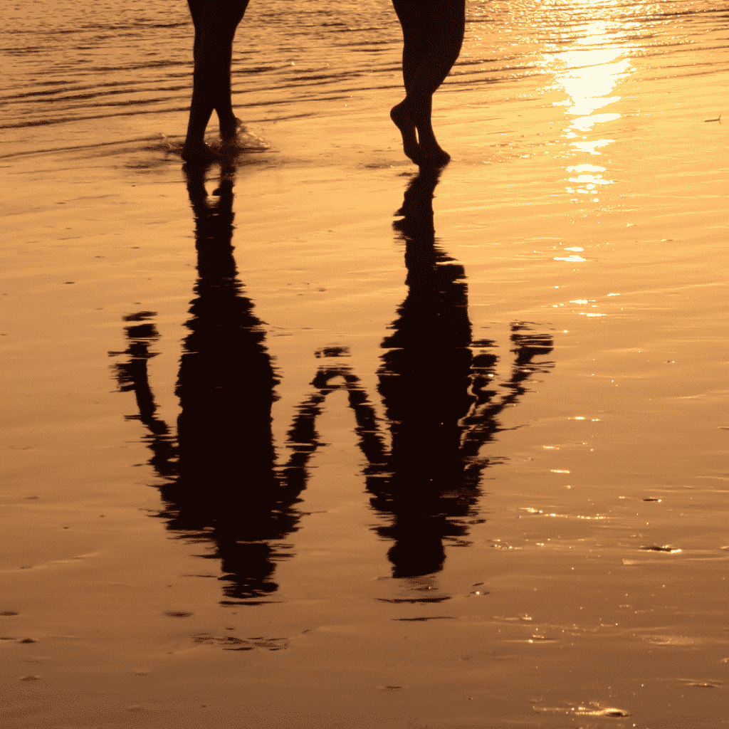 Reflexo na água de duas pessoas andando na praia juntas