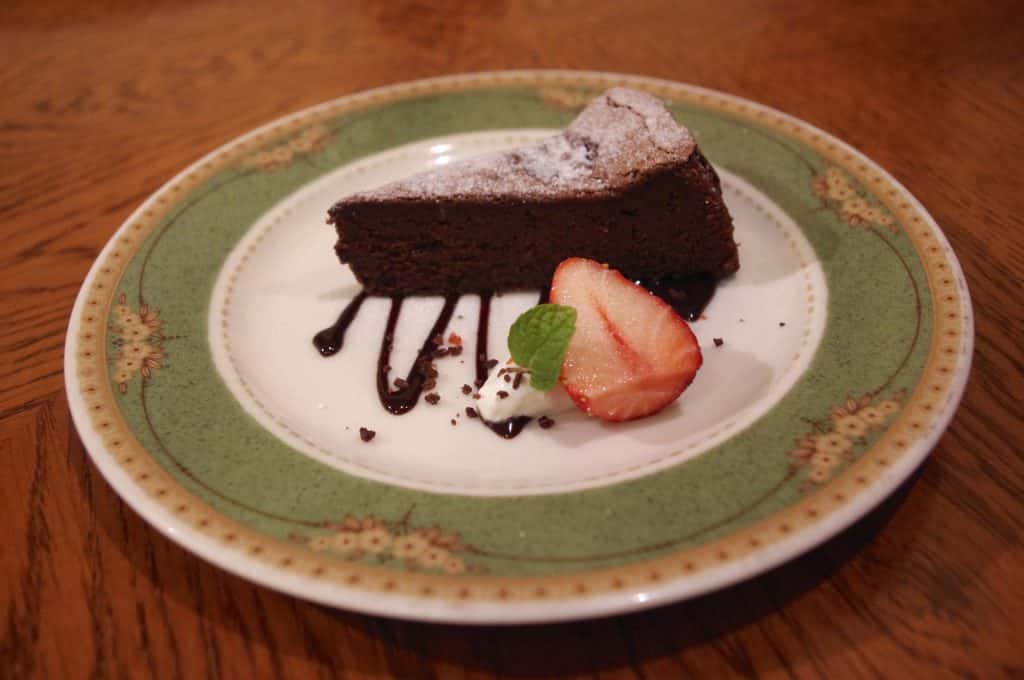 Imagem de um pedaço de brownie de chocolate low carb disposto em um prato de porcelana decorado com um pedaço de morango com hortelã.