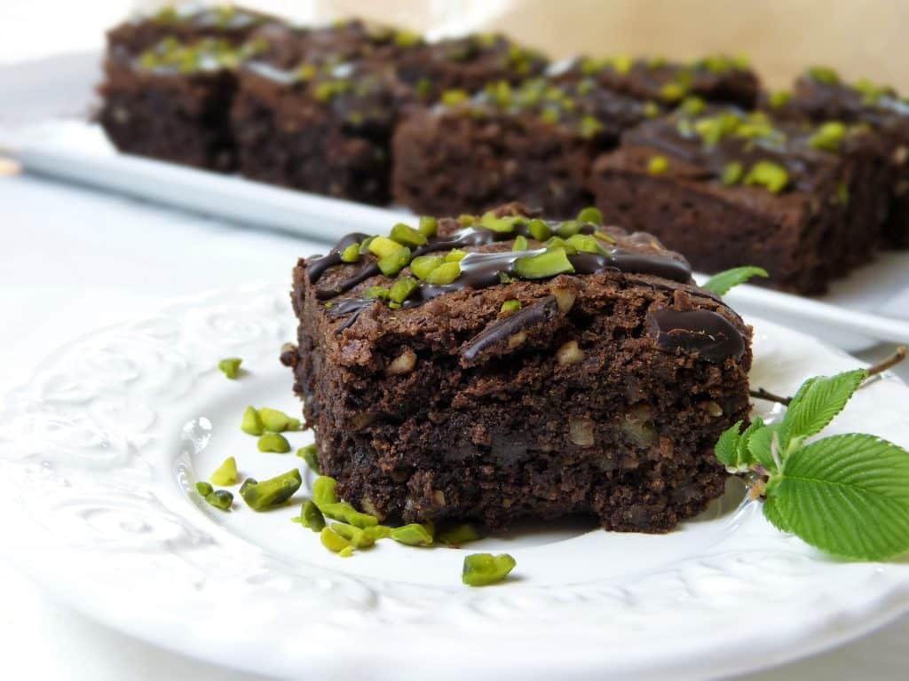 Imagem de um prato e uma travessa de porcelana branco e neles pedaços de brownie de chocolate sem glúten decorados com folhas de hortelã.
