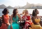 Quatro mulheres, sendo duas brancas e duas negras, sentadas num barco olhando para o lado.