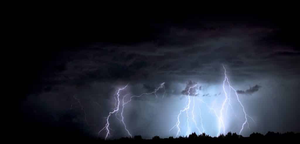 Imagem de muitas nuvens escuras no céu e entre elas muitos raios anunciando uma tempestade.
