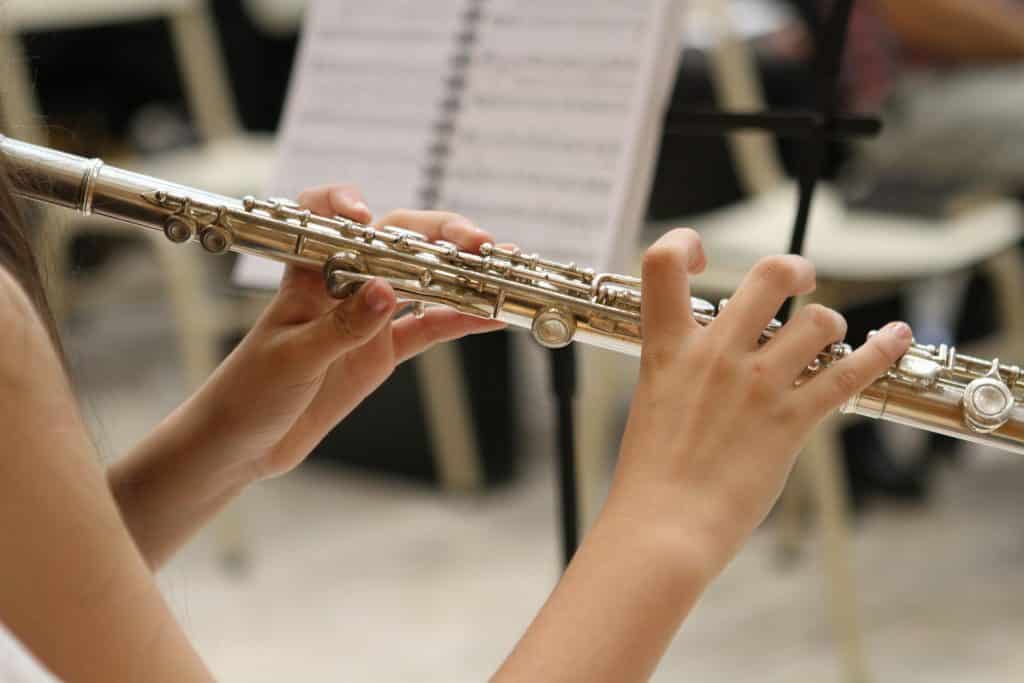 Imagem de uma moça sentada tocando uma flauta na cor dourada.
