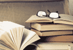 Pilha de livros com óculos acima de livro aberto