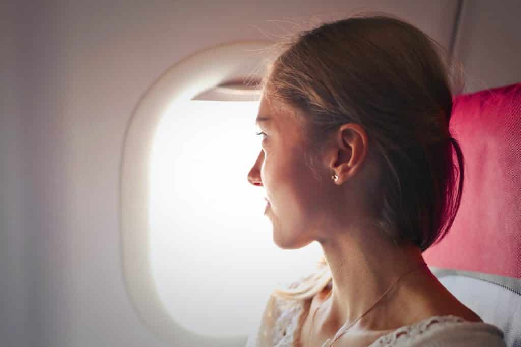 Menina loira dentro do avião olhando pela janela 