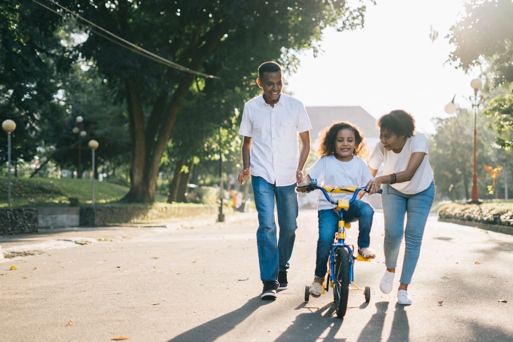 Pais ensinam filha a andar de bicicleta.