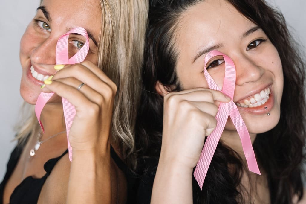 Duas mulheres sorriem enquanto seguram laços cor de rosa representativos da luta contra o câncer de mama.