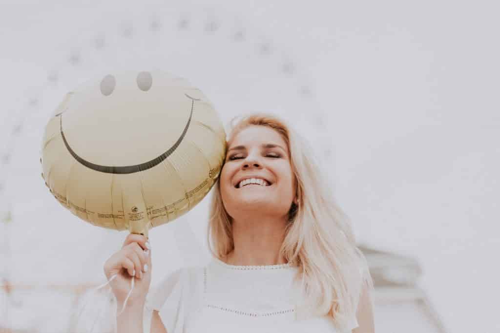 Mulher sorrindo enquanto segura um balão amarelo que também está sorrindo 