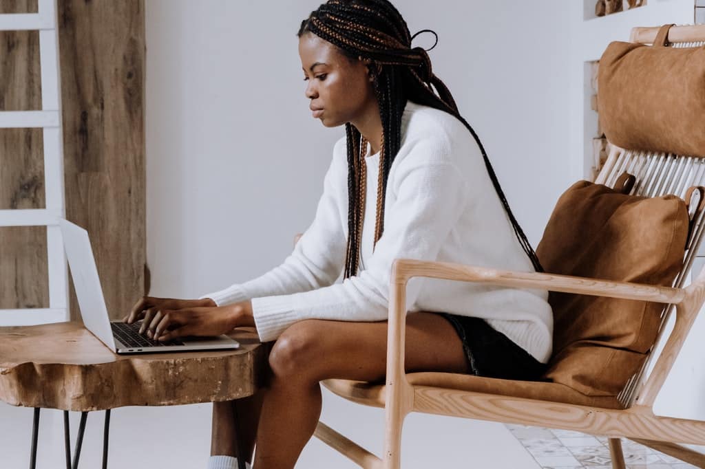 Mulher sentada em cadeira enquanto digita em um computador.