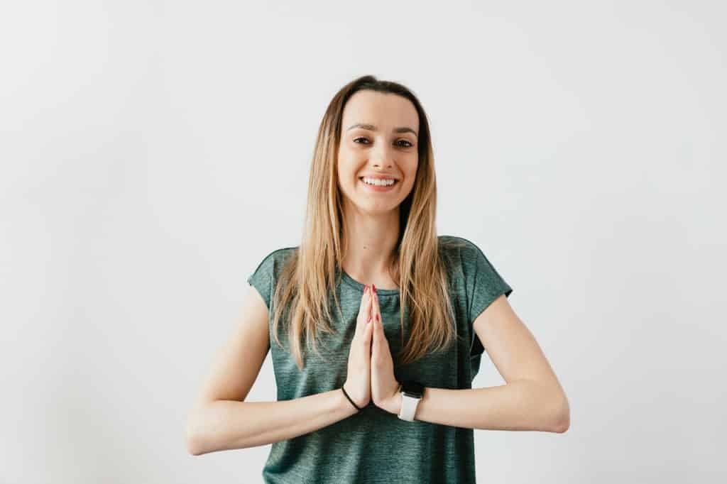 Mulher sorrindo com as mãos unidas próximas do peito.