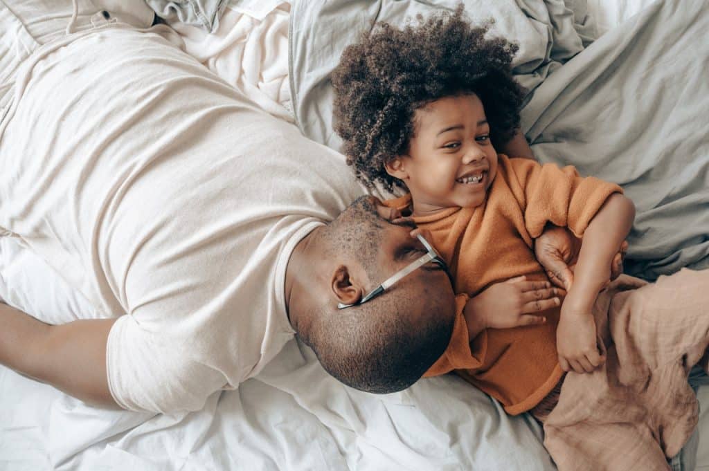 Pai e filho deitados na cama brincando 