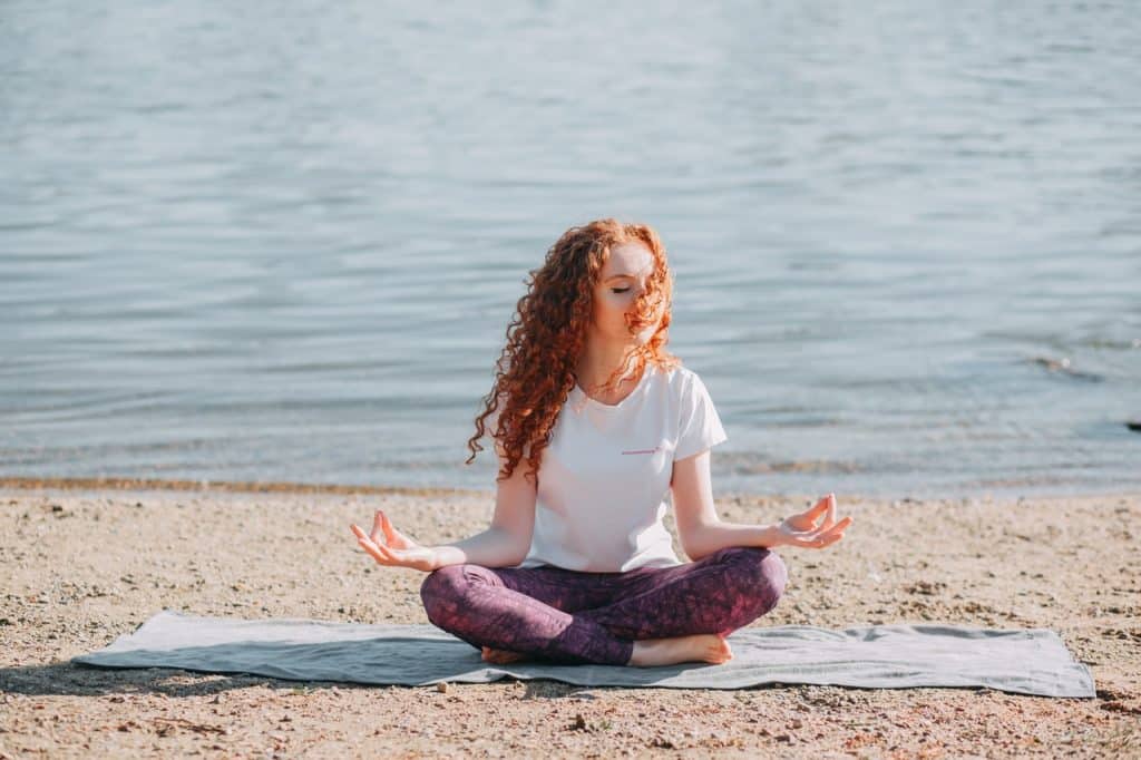 Mulher sentada em posição de meditação em uma praia.