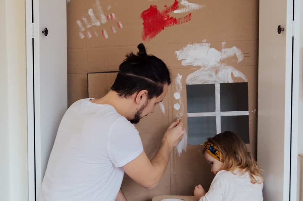 Homem adulto e menina pintam papelão.