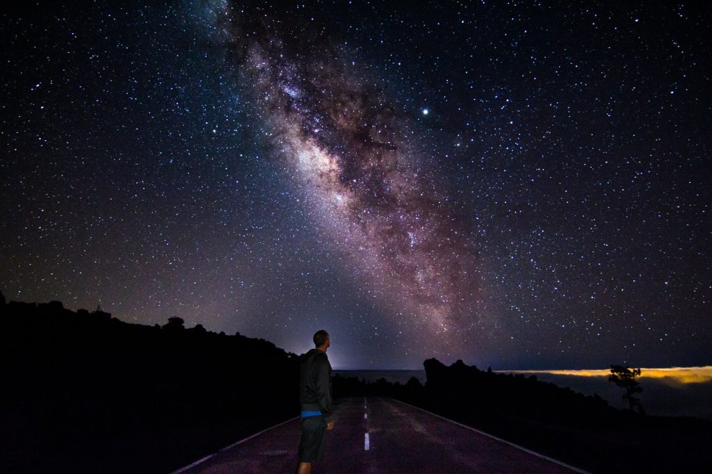 Homem em uma estrada olhando para o céu e o céu está estrelado com um desenho de galáxia.