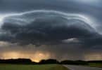 Imagem de um rodovia livre e ao lado um gramado bem verdinho. Ao fundo a formação de uma tempestade formada por um nuvem bem carregada e escura.