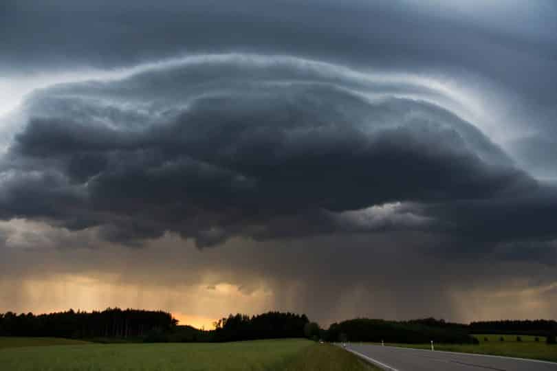 Imagem de um rodovia livre e ao lado um gramado bem verdinho. Ao fundo a formação de uma tempestade formada por um nuvem bem carregada e escura.