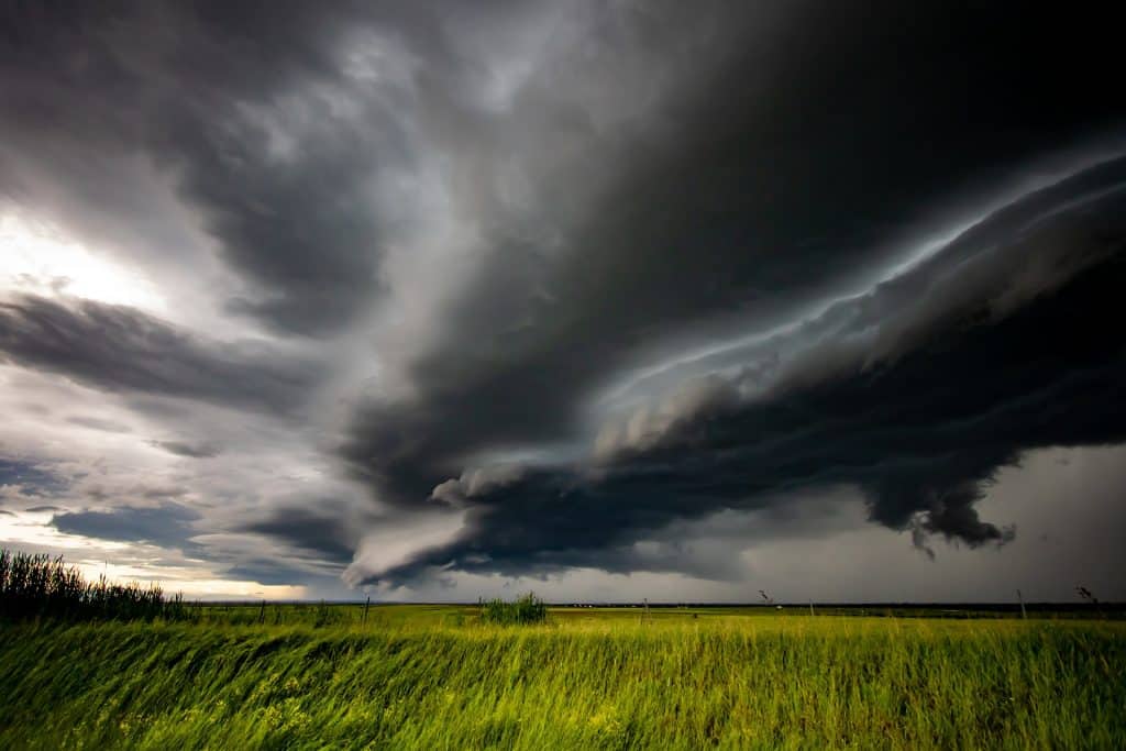 Imagem de um campo verde. No céu est´se formando uma nuvem escura e bem espessa de tempestade com muita ventania.