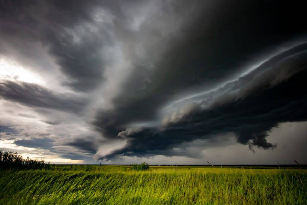 Imagem de um campo verde. No céu est´se formando uma nuvem escura e bem espessa de tempestade com muita ventania.
