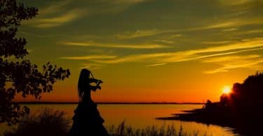 Imagem de uma violinista tocando uma música em frente a um lindo por do sol.
