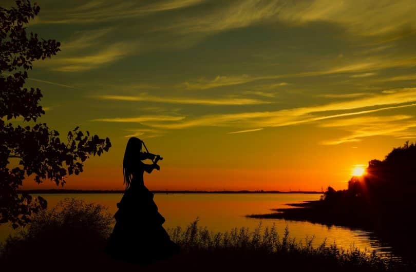 Imagem de uma violinista tocando uma música em frente a um lindo por do sol.