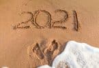 Número 2021 escrito na areia. Marcas de pés estão abaixo, seguidos por água de mar.