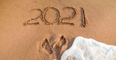 Número 2021 escrito na areia. Marcas de pés estão abaixo, seguidos por água de mar.
