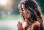 Mulher jovem medita, praticando ioga na natureza com as mãos em posição de oração.