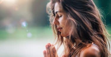 Mulher jovem medita, praticando ioga na natureza com as mãos em posição de oração.