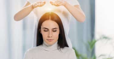 Mulher branca com mãos sobre cabeça de mulher branca sentada.