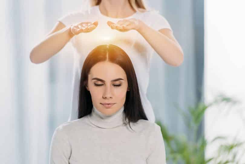 Mulher branca com mãos sobre cabeça de mulher branca sentada.