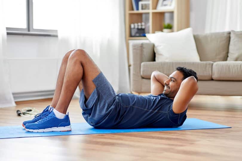 Homem branco fazendo abdominais no chão.