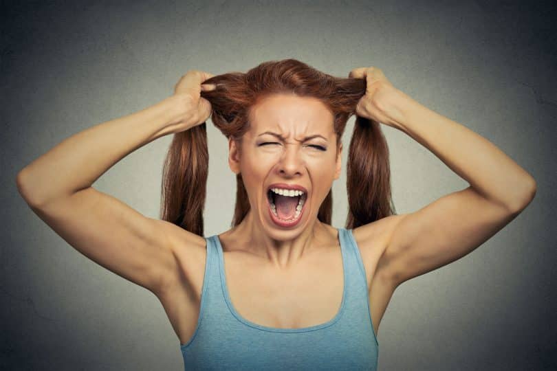 Mulher com a expressão facial estressada e mãos segurando os cabelos.