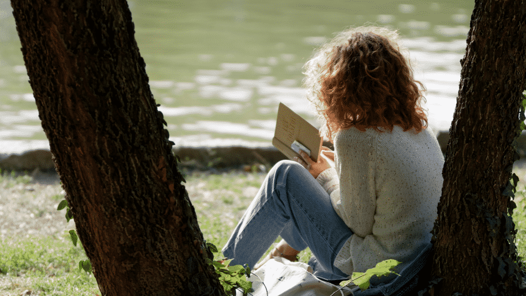 Mulher de costas sentada embaixo da árvore lendo um livro