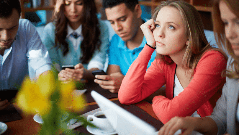 Menina pensativa no meio de pessoas mexendo no celular