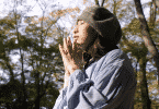 Mulher de chapéu com os olhos fechados fazendo um pedido no meio da floresta