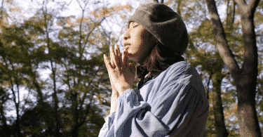 Mulher de chapéu com os olhos fechados fazendo um pedido no meio da floresta