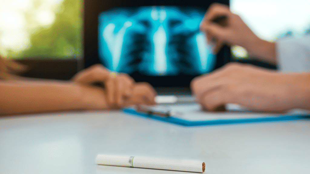 Foto de um cigarro e, ao fundo, uma pessoa e um médico conversando sobre o raio-x do pulmão