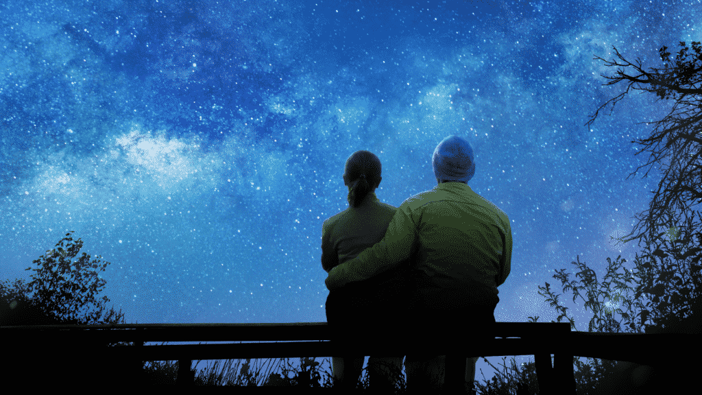 Silhueta de casal abraçados observando o céu noturno estrelado