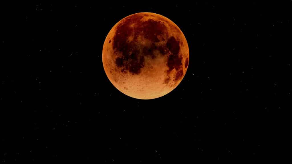 Imagem da super lua na cor alaranjada e ao fundo o céu estrelado.