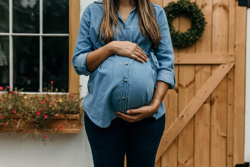 Mulher negra com as mãos ao redor da barriga de grávida.