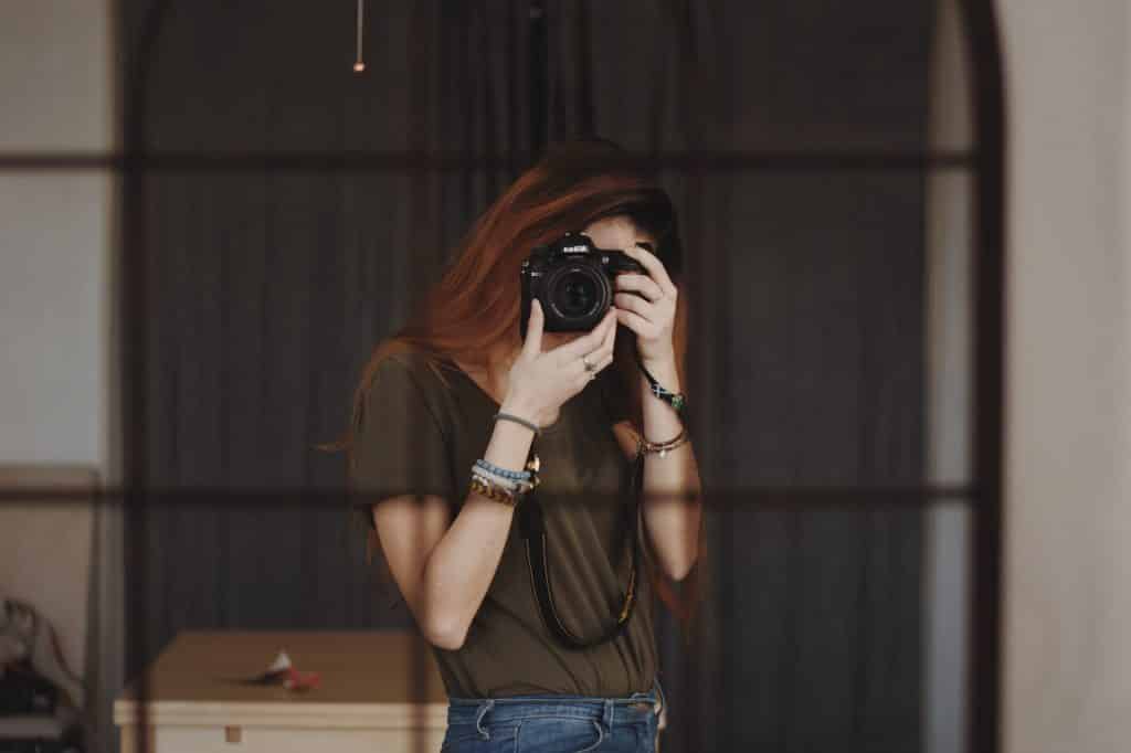 Mulher branca segurando câmera fotográfica em frente ao rosto.