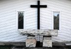 Imagem de fundo branco e em destaque uma cruz na cor preto e o lado dois quadros. À frente um mesa de pedra, representando o altar de uma igreja preparado para a quaresma.