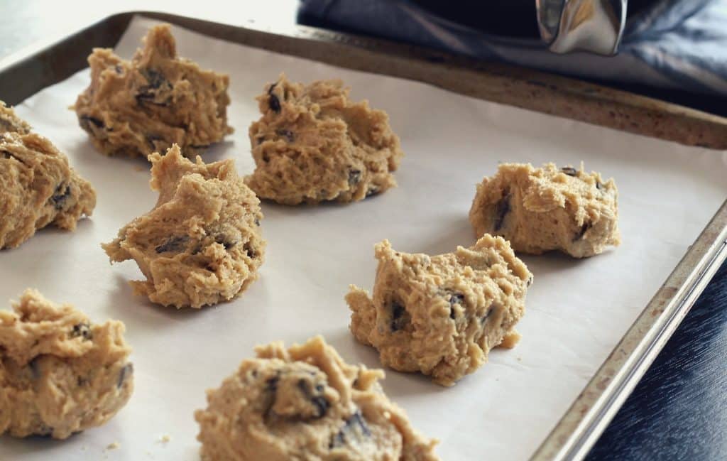 Imagem de uma travessa de alumínio forrada com papel manteiga e sobre ela vários cookies indo para o forno.
