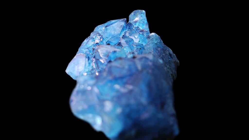 Imagem de fundo preto e em destaque um lindo cristal de água-marinha na cor azul.