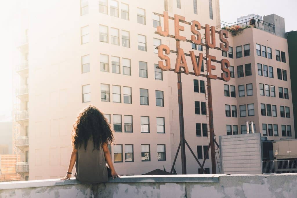 Mulher negra de costas sentada no parapeito de um prédio.